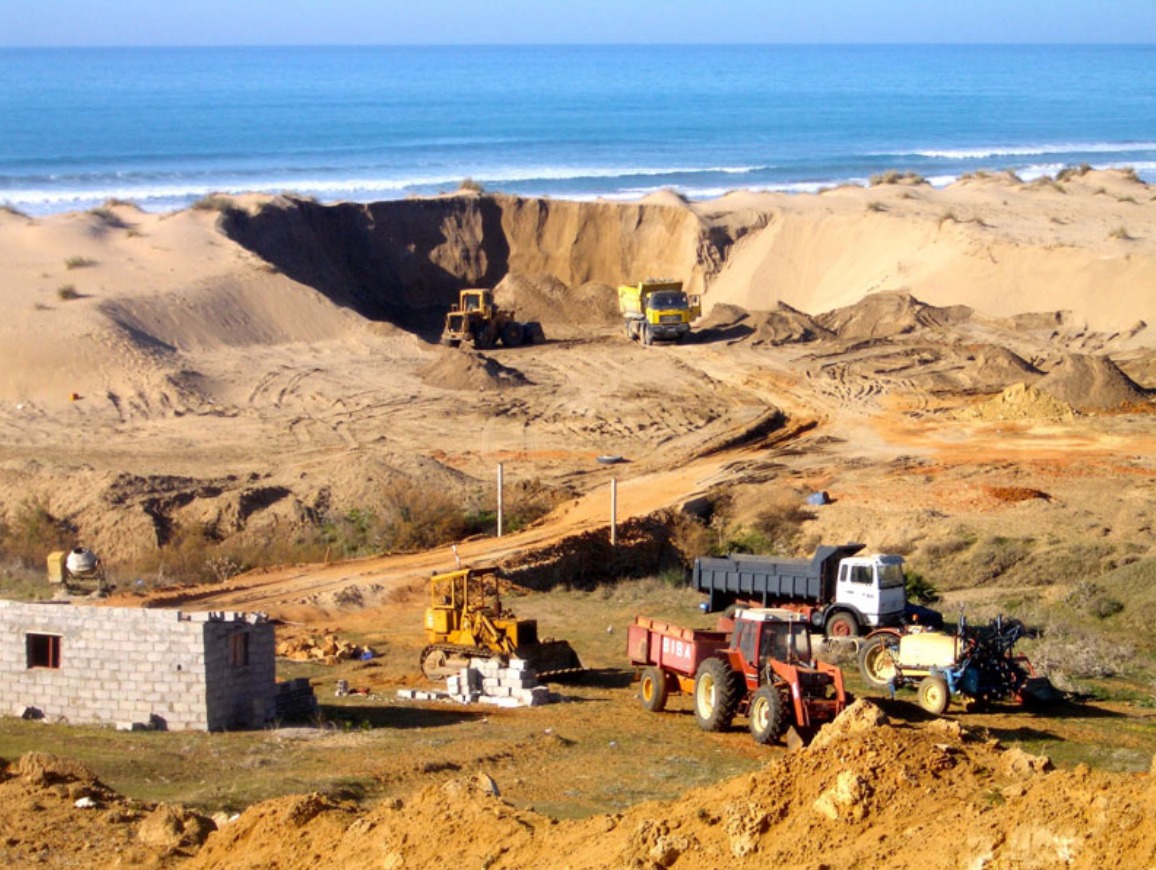 Des camions s'activant dans une carrière sauvage de sable de plage au Maroc