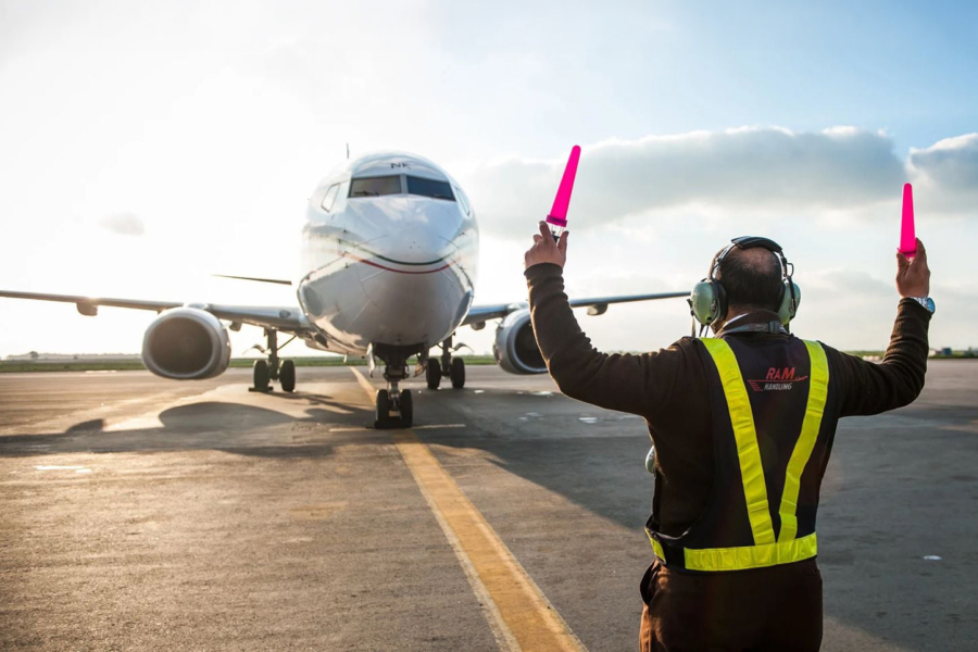 Un agent de piste de RAM Handling guidant un avion sur le tarmac.